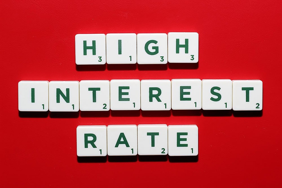 Bokstavsbrickor som stavar 'HIGH INTEREST RATE' på en röd bakgrund, vilket symboliserar de höga insatserna i räntepolitiken.